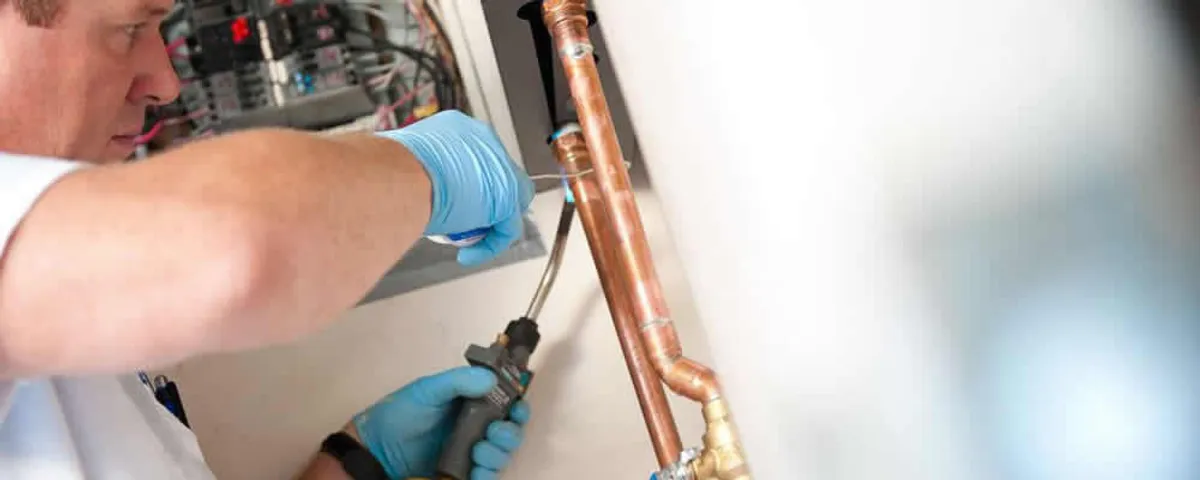 Water heater repair technician testing copper pipe connections and controls in Glendale, AZ
